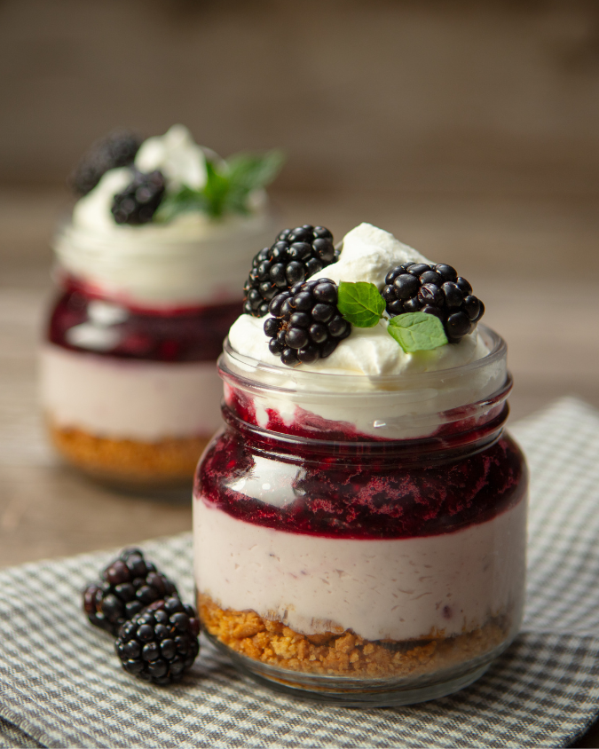 Blackberry mini cheesecake trifles in mason jars for a summer dessert on a rustic background